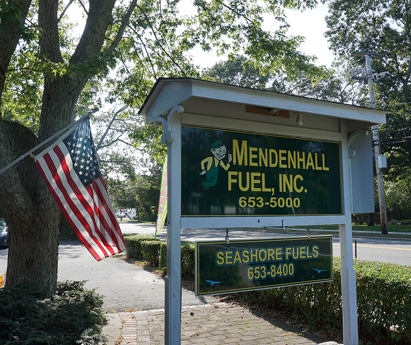 Mendenhall Fuel outdoor business sign with trees and the American flag